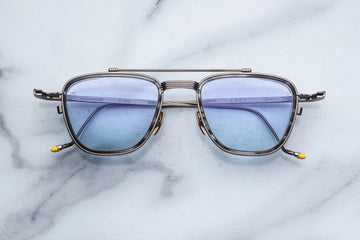 Matte gunmetal metal aviator frame with blue lenses on a white marble background