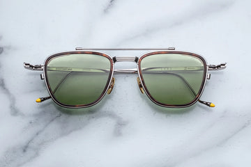 Antique silver metal aviator frame with green lenses on a white marble background