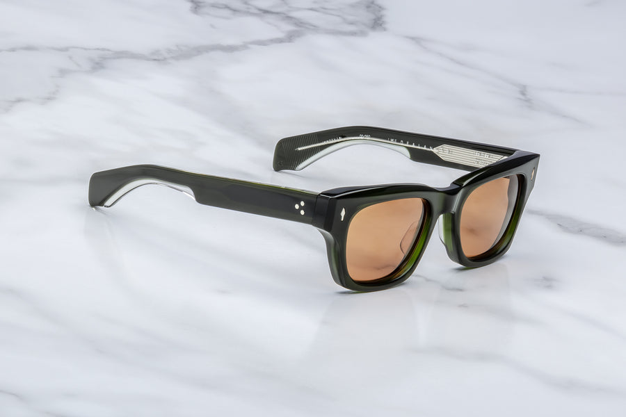 Side profile of green acetate sunglasses with orange lenses and visible silver wirecore, across a marble background