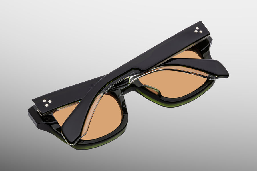 Dark green sunglasses with orange lenses and crystal highlights, lens down against a grey backdrop 