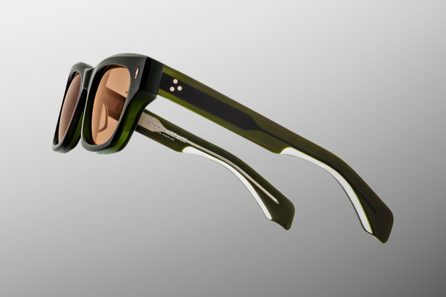 Side view of green acetate sunglasses with orange lenses floating against a grey backdrop