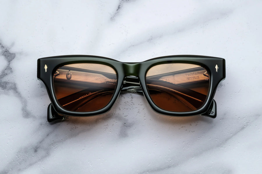 Dark green acetate sunglasses with orange lenses across a white marble background