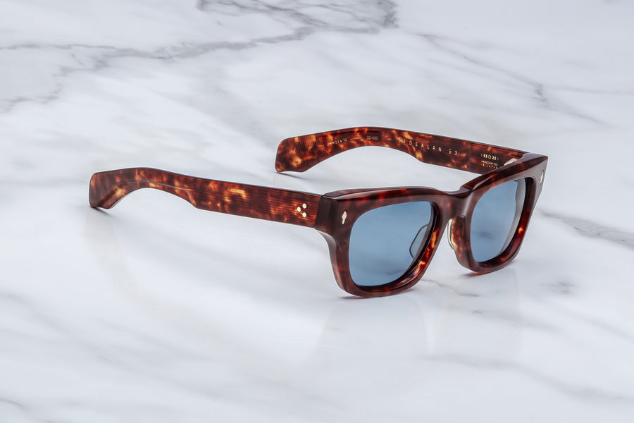 Side profile of brown tortoiseshell acetate sunglasses with blue lenses, across a marble background