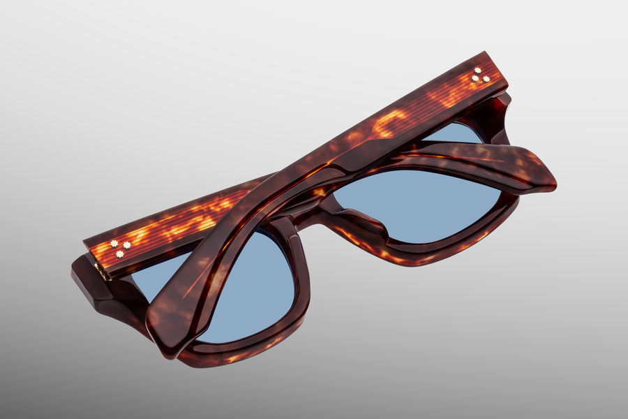 Brown tortoiseshell sunglasses with blue lenses, lens down against a grey backdrop 