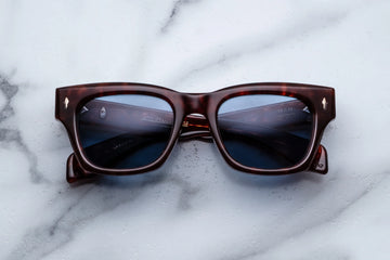 Brown tortoiseshell acetate sunglasses with blue lenses across a white marble background