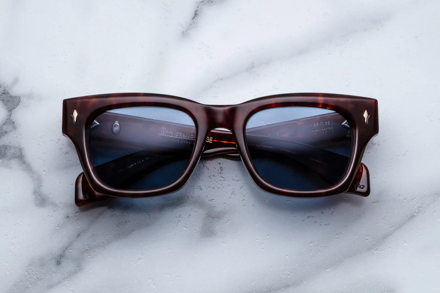 Brown tortoiseshell acetate sunglasses with blue lenses across a white marble background
