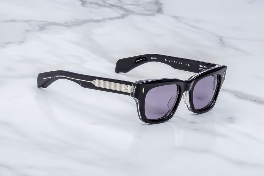 Side profile of dark blue acetate sunglasses with purple lenses and visible silver wirecore, across a marble background