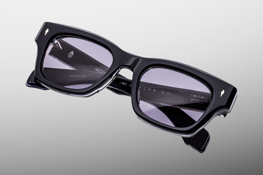 Dark blue acetate sunglasses with purple lenses against a grey background