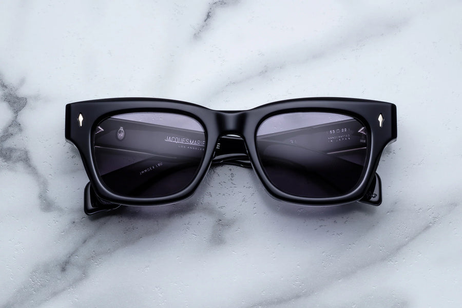 Dark blue acetate sunglasses with purple lenses across a white marble background