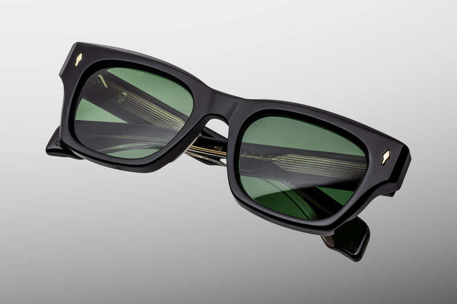Black acetate sunglasses with green lenses and silver hardware against a grey background
