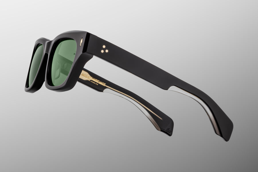 Side view of black acetate sunglasses with green lenses floating against a grey backdrop