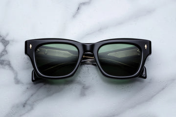 Black acetate sunglasses with green lenses across a white marble background