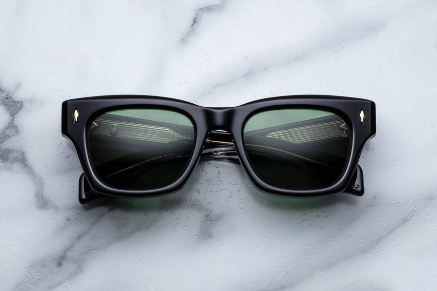 Black acetate sunglasses with green lenses across a white marble background