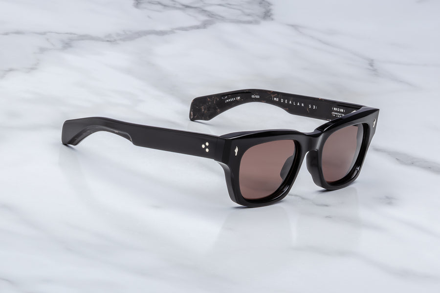 Side view of black sunglasses with brown lenses on a marble surface