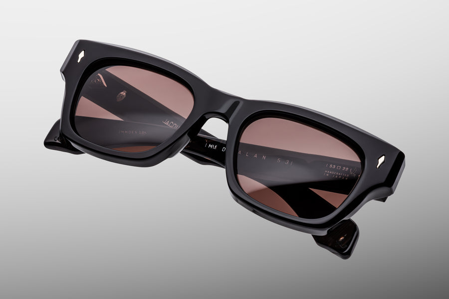 Thick black acetate sunglasses with brown lenses on a grey background