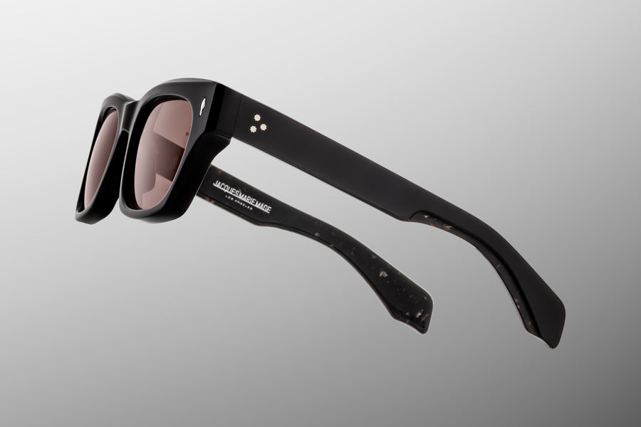 Side profile of thick black acetate sunglasses with brown lenses against a grey background