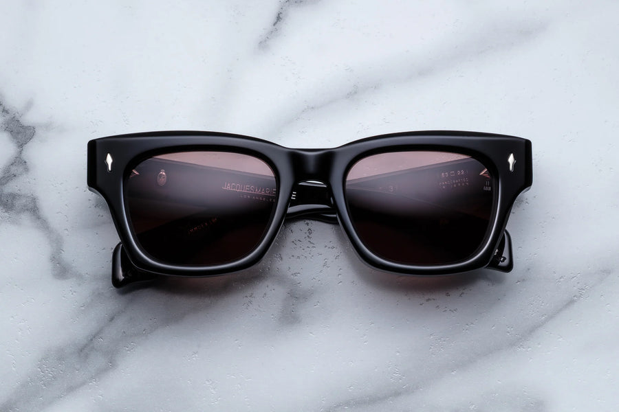 Thick black acetate frame with deep brown sunglass lenses on a white marble background