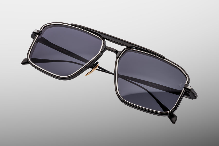 Sunglasses with a black and silver metal frame with dark grey lenses on a grey background