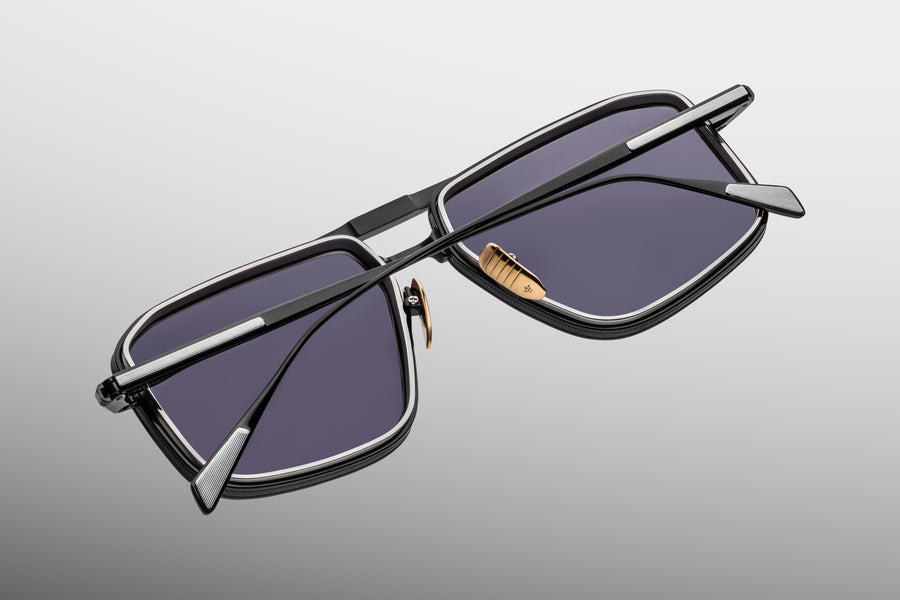 Sunglasses with a black and silver metal frame with dark grey lenses on a grey background