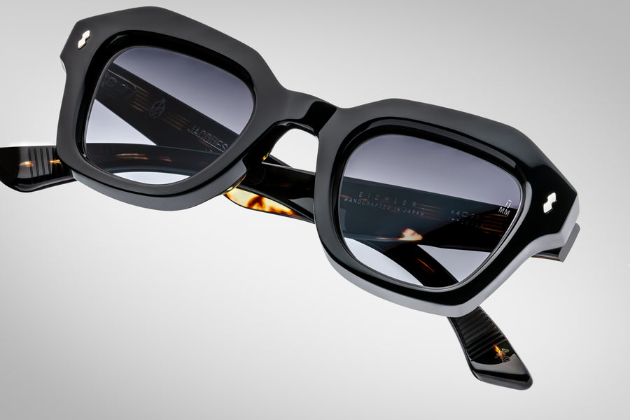 Black square sunglasses with a reflective surface and accents of tortoiseshell on the temples, on top a light grey background.