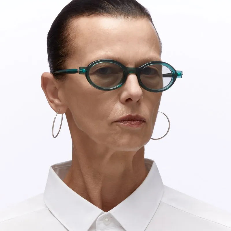 Person wearing green eyeglasses and a white shirt on a plain background