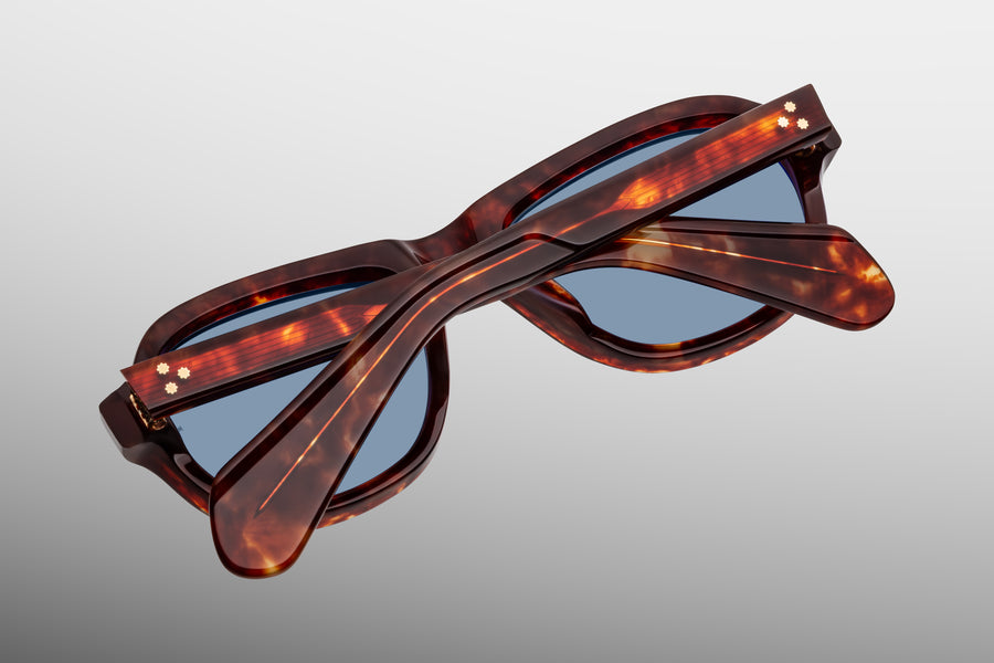 Back view of a brown tortoiseshell acetate acetate aviator sunglass, with temples folded over one another and blue lenses visible.