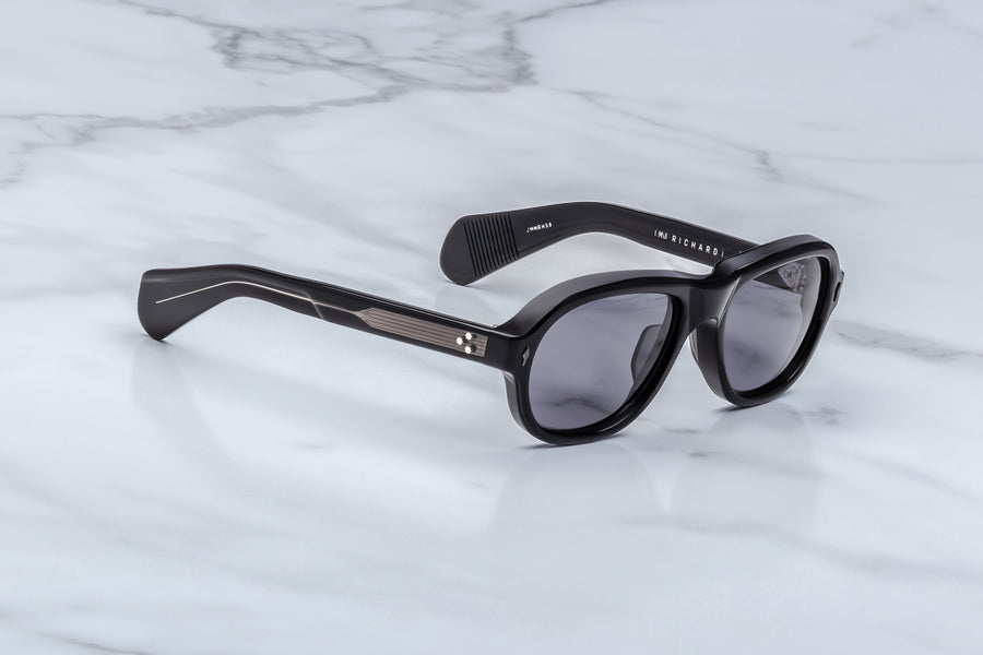 3/4 angle of round aviator style sunglass frames, in black acetate and grey lenses, with gunmetal hardware.