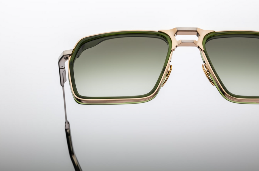 Sunglasses with gold frame and green-tinted lenses on a light gray background