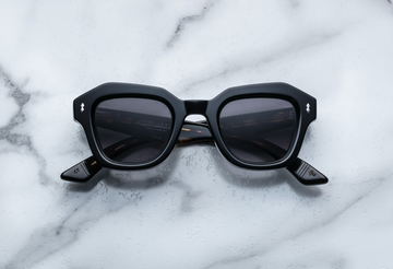 Black square sunglasses with silver hardware, front facing on a white marble background