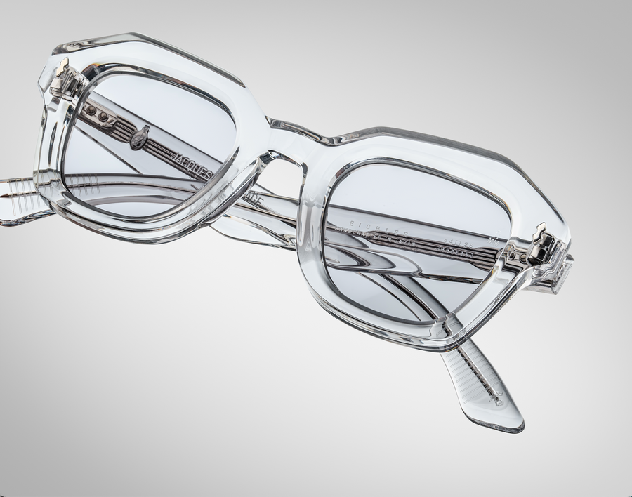 Clear sunglasses with light grey lenses and silver hardware, on top of a light grey background.