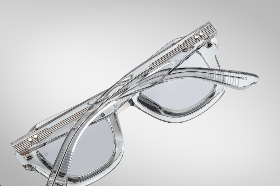 Crystal sunglasses with exposed silver hardware on the temples, folded over and pictured laying lens side down on a grey background.