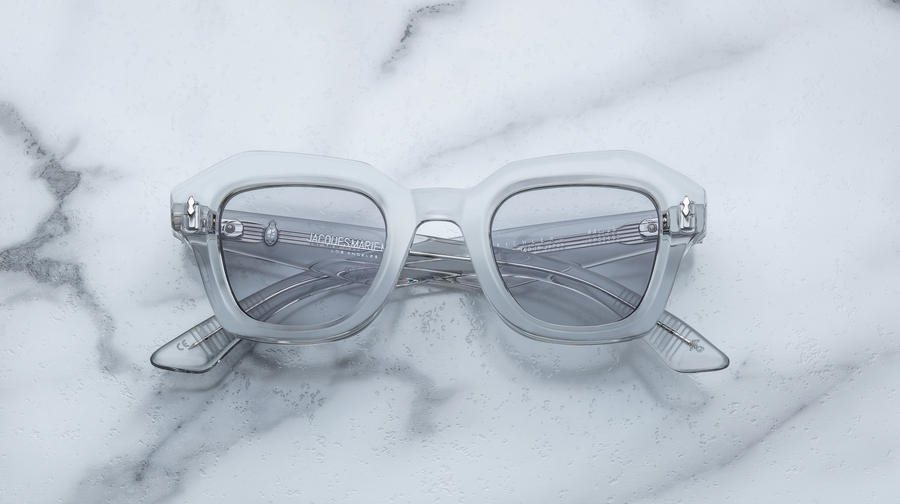 Grey transparent sunglasses with silver hardware, front facing on a white marble background.