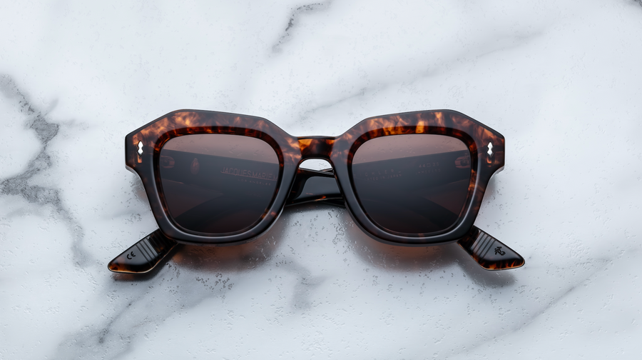 Brown tortoiseshell sunglasses with silver hardware, front facing on a white marble background.