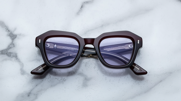 Dark red sunglasses with silver hardware, front facing on a white marble background.