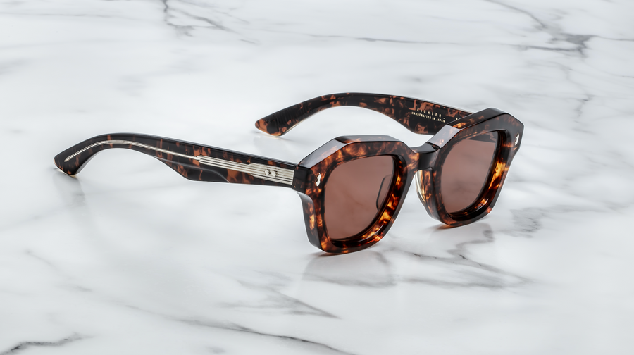 Brown tortoiseshell sunglasses with exposed silver hardware, at a 3/4 angle on top of a white marble background.