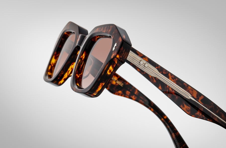 Close up of a profile view of brown tortosieshell sunglasses, with exposed silver hardware on the temples.