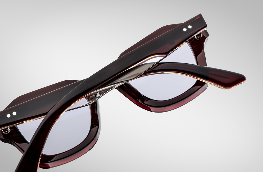 Behind view of dark red sunglasses with clear accents, with temples folded over and pictured laying lens side down on a grey background.