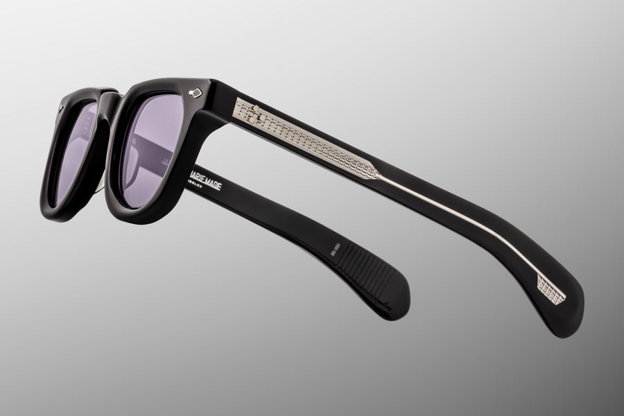 Black sunglasses with purple lenses and exposed decorative silver hardware against a grey background
