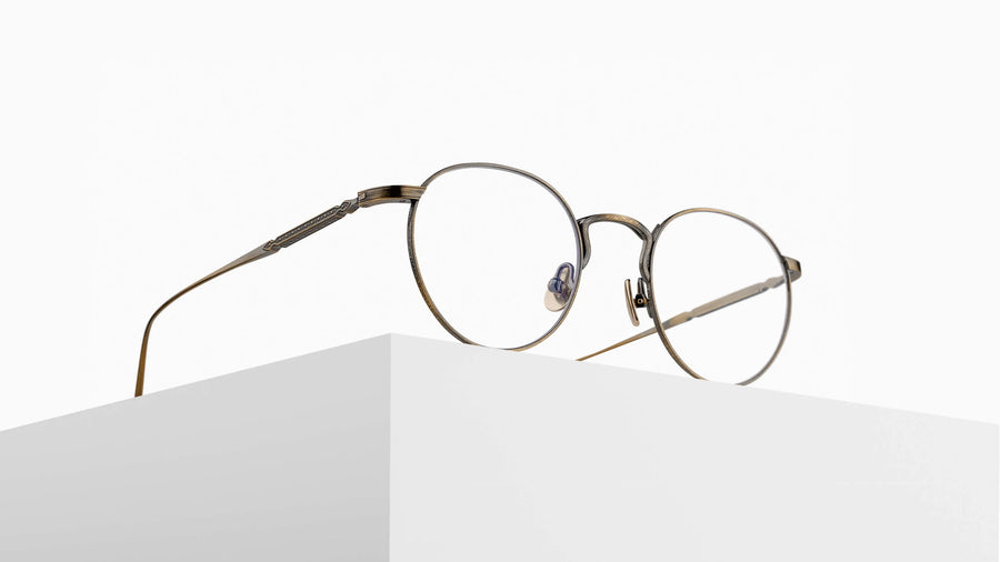 Round antique gold metal eyeglasses on a pedestal against a white background