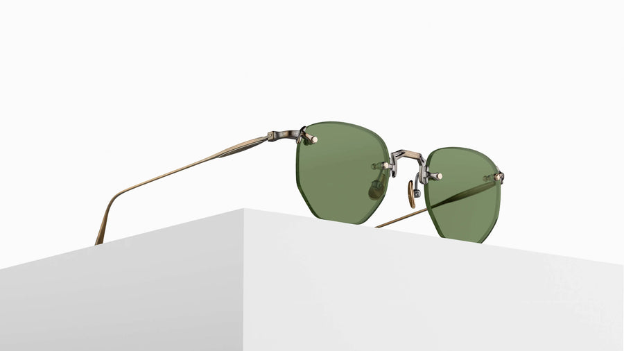 Gold framed rimless sunglasses with dark green lenses on a grey pedestal 